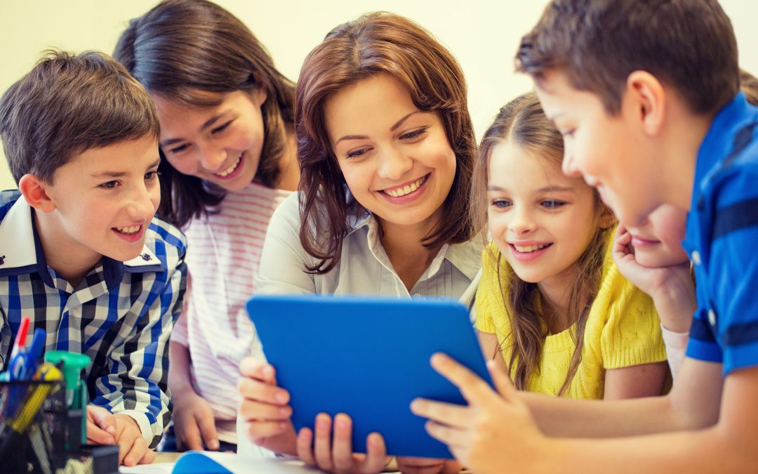 Maestra con un grupo de alumnos con actitud sonriente mientras miran una tablet.